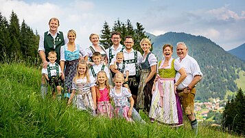 Große Gastgeberfamilie des Spa- & Familien-Resorts Krone im Allgäu steht in Tracht in der Wiese.