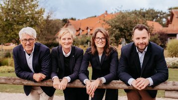 Die Gastgeber des Landhaus Averbeck lehnen lächelnd an einem Holzzaun vor der Hofanlage.