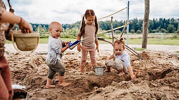 Kinder spielen mit Spielsachen im Sandkasten auf dem Außengelände des Familienhotels Landhaus Averbeck in der Lüneburger Heide.