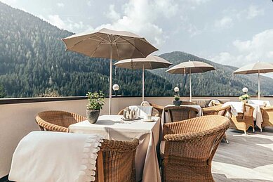 Sonnenterrasse mit Rattanmöbeln und Sonnenschirmen im Familienhotel Engel Gourmet & Spa in Südtirol.