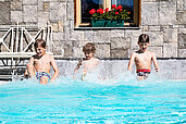 3 Kinder sitzen am Beckenrand vom Pool und planschen mit den Beinen im Basser vom Familienhotel Hotel Tirolerhof an der Zugspitze.