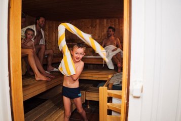 Junge wedelt mit einem Handtuch in der Luft in der Familiensauna des Familienhotels Kirchheimerhof in Kärnten.
