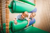 Zwei Kinder haben Spaß im Indoor-Spielbereich des Landguts Furtherwirt und klettern lachend durch weiche, grüne Hindernisse