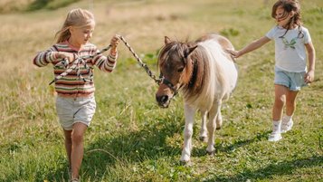 Zwei Kinder führen ein Pony über eine Wiese beim Hotel Bella Vista in Südtirol.