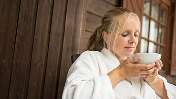 Eine Frau im Bademantel trinkt eine Tasse Tee im Familienhotel Ottonenhof im Sauerland