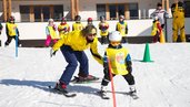 Kind fährt mit Skilehrerin beim Skikurs im Familienhotel Ramsi durch einen Parcours im Schnee.