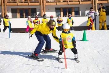 Kind fährt mit Skilehrerin beim Skikurs im Familienhotel Ramsi durch einen Parcours im Schnee.