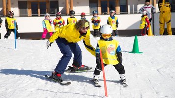 Kind fährt mit Skilehrerin beim Skikurs im Familienhotel Ramsi durch einen Parcours im Schnee.