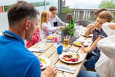 Eine Familie sitzt beim Abendessen zusammen an einem Tisch auf der Terrasse des Hotels Alpengasthof Hochegger. 