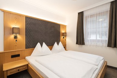 Elternschlafbereich im Familienhotel Oberkarteis mit Doppelbett, Holzdetails und gemütlicher Beleuchtung im alpinen Stil.