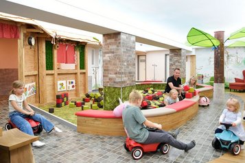 Kinder fahren mit Bobbycars durch den fantasievollen Indoor-Spielbereich mit Themenhäusern und Baustein-Areal im Familienhotel Rhön Feeling.