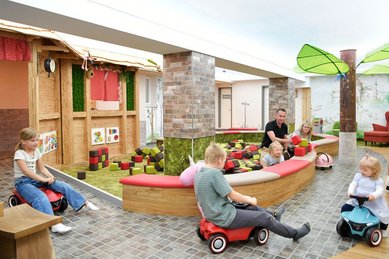 Kinder fahren mit Bobbycars durch den fantasievollen Indoor-Spielbereich mit Themenhäusern und Baustein-Areal im Familienhotel Rhön Feeling.