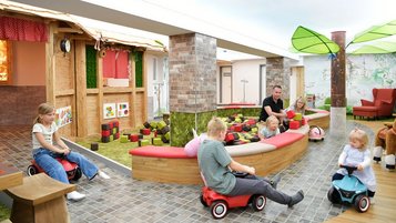 Kinder fahren mit Bobbycars durch den fantasievollen Indoor-Spielbereich mit Themenhäusern und Baustein-Areal im Familienhotel Rhön Feeling.
