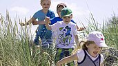 Vier Kinder laufen glücklich durch die Dünen am Strand im Familienurlaub an der Nordsee.