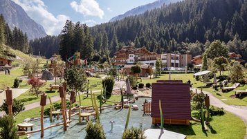 Außenansicht des Familienhotel Habachklause im Sommer mit großem Abenteuerspielplatz und umliegender Bergkulisse.