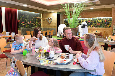 Vierköpfige Familie sitzt am Frühstückstisch im Restaurant des Familienhotels Rhön Feeling und genießt entspannt ihr Frühstück.