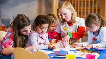 Kinder malen und basteln gemeinsam mit einer Betreuerin im Zauchenseehof, umgeben von bunten Stiften und kreativen Materialien