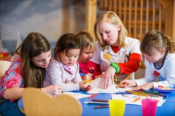 Kinder malen und basteln gemeinsam mit einer Betreuerin im Zauchenseehof, umgeben von bunten Stiften und kreativen Materialien