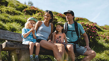 Familie sitzt auf einer Holzbank mitten in der Natur und genießt die Aussicht.