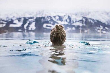 Frau schwimmt im Outdoor Pool des Allgäuer Berghofs mit Blick in die beschneiten Berge.