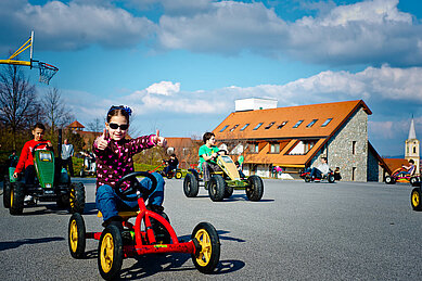 Kinder fahren mit ihren Karts ein Rennen auf dem Hof vom Familienhotel Kolping Hotel Spa & Family Resort in Ungarn.