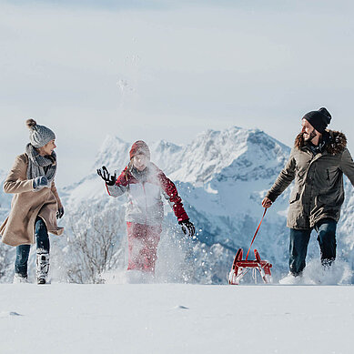 Winter im Salzburger Land: Familie macht eine Winterwanderung mit einem Schlitten. Bergpanorama im Hintergrund.