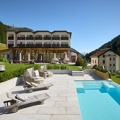 Außenansicht des Familienhotels Bella Vista in Südtirol im Sommer. Vor dem Hotel befinden sich ein Outdoor-Pool und Sonnenliegen.