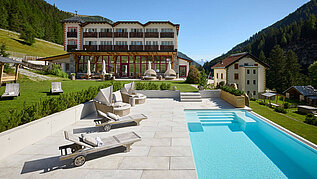Außenansicht des Familienhotels Bella Vista in Südtirol im Sommer. Vor dem Hotel befinden sich ein Outdoor-Pool und Sonnenliegen.