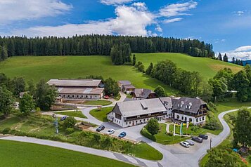 Außenansicht des Familienhotels Der Ponyhof in der Steiermark. Das Hotel ist umgeben von einem großzügigen Außenbereich mit viel Platz für die Kinder zum Spielen.