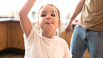 Familotel All-Inclusive Verpflegung für Kinder: Mädchen isst eine Spagetti. Im Hintergrund Papa und das Buffet