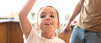 Familotel All-Inclusive Verpflegung für Kinder: Mädchen isst eine Spagetti. Im Hintergrund Papa und das Buffet