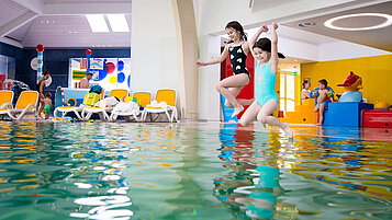 Zwei Kinder springen vom Beckenrand in das Schwimmbecken im Familienhotel Kolping Hotel Spa & Family Resort in Ungarn.