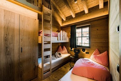 Gemütliches Schlafzimmer mit Holzvertäfelung, Etagenbett, Einzelbett und rot-weiß karierten Kissen in einem familienfreundlichen Chalet im Alpura Retreat.