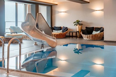 Indoor-Pool im Familienhotel Amiamo mit Edelstahlrutsche und gemütlichen Ruheliegen für entspannte Familienmomente.