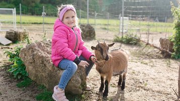 Ein kleines Mädchen streichelt eine Ziege auf dem Gelände vom Familienhotel Friedrichshof.