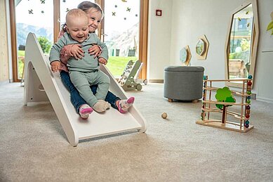 Baby rutscht mit großer Schwester auf der Babyrutsche im Happy-Club im Familienhotel Almfamilyhotel Scherer in Tirol.