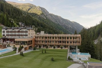 Außenansicht des Familienhotel Bella Vista in Südtirol mit Neubau, großer Wiese, Poolbereich und Bergkulisse.