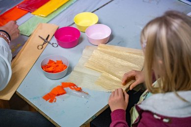 Kinder basteln mit buntem Papier und Scheren in der kreativen Kinderbetreuung des Familienhotels Bruckwirt.