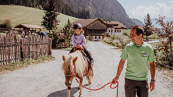 Mädchen sitzt auf einem Pony und wird von einem Kinderbetreuer geführt.