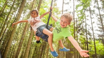 Zwei fröhliche Kinder beim Schaukeln im Wald während der Kinderbetreuung im Landhaus zur Ohe