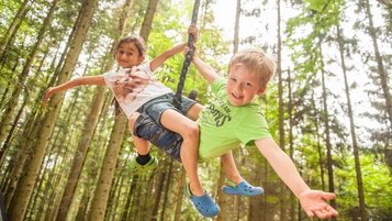 Zwei fröhliche Kinder beim Schaukeln im Wald während der Kinderbetreuung im Landhaus zur Ohe