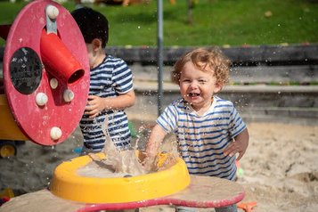 Kinder spielen lachend mit Wasser und Sand auf dem Outdoor Spielplatz des Familienhotels Ramsi in Kärnten