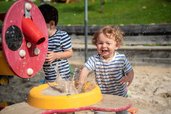 Kinder spielen lachend mit Wasser und Sand auf dem Outdoor Spielplatz des Familienhotels Ramsi in Kärnten