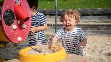 Kinder spielen lachend mit Wasser und Sand auf dem Outdoor Spielplatz des Familienhotels Ramsi in Kärnten