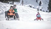 Familienhotel Alpenhof Dolomit Family im Winter. Familie hat beim gemeinsamen Rodeln Spaß.