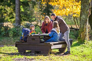 Eine Gastfamilie vom Familienhotel Am Rennsteig sitzt im Thüringer Wald auf einer Sitzbank und legen eine Pause ein.