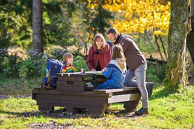 Eine Gastfamilie vom Familienhotel Am Rennsteig sitzt im Thüringer Wald auf einer Sitzbank und legen eine Pause ein.