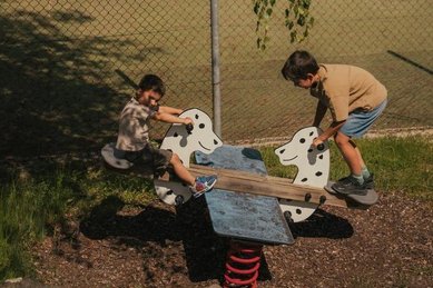Zwei Kungs sitzen auf einer Wippe auf dem Spielplatz des Familienhotels Engel Gourmet & Spa in Südtirol