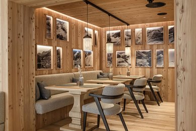 Gemütlicher Stubenbereich im Hotel Zauchenseehof mit hochwertiger Holzvertäfelung, bequemen Polsterbänken, eleganten Holztischen und stimmungsvoll beleuchteten Bergfotografien an den Wänden.