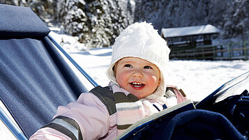 Kleinkind sitzt im Winter auf einer Liege auf dem Außengelände des Familienhotels Habachklause.